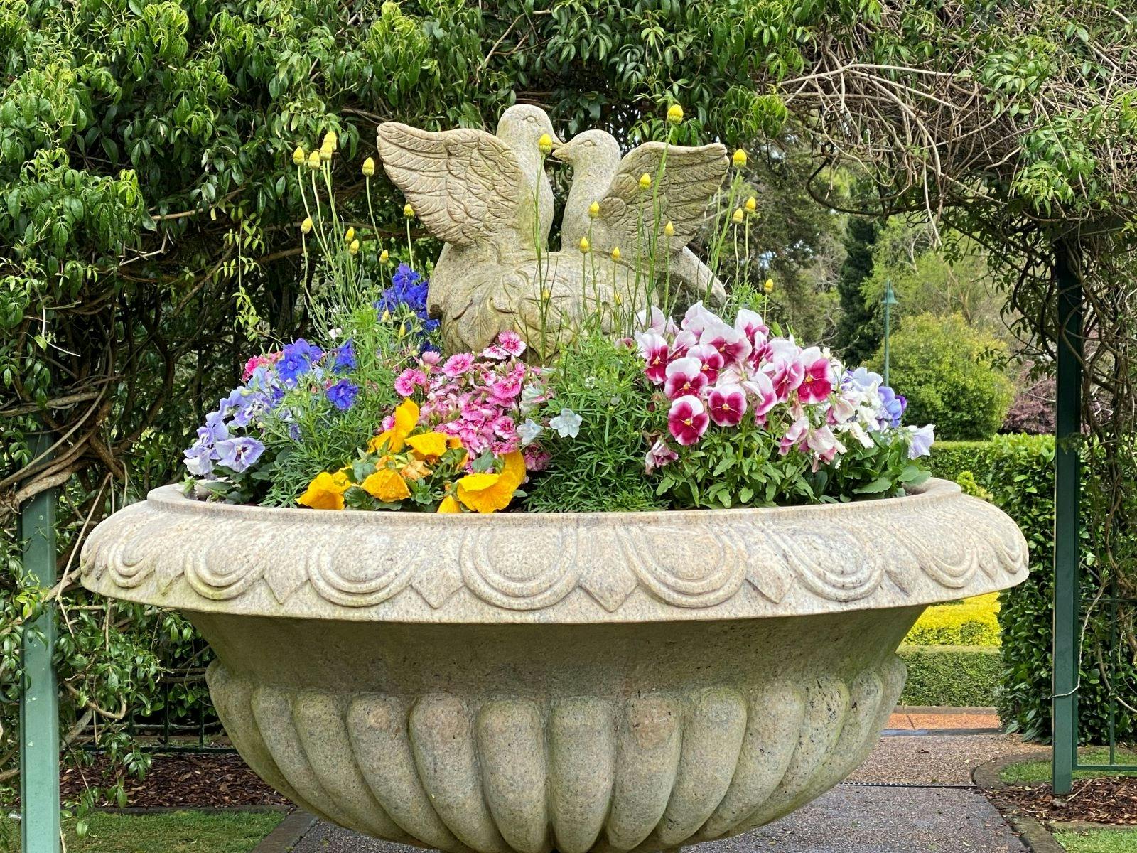 Statue of two doves surrounded by blue, yellow and pink flowers