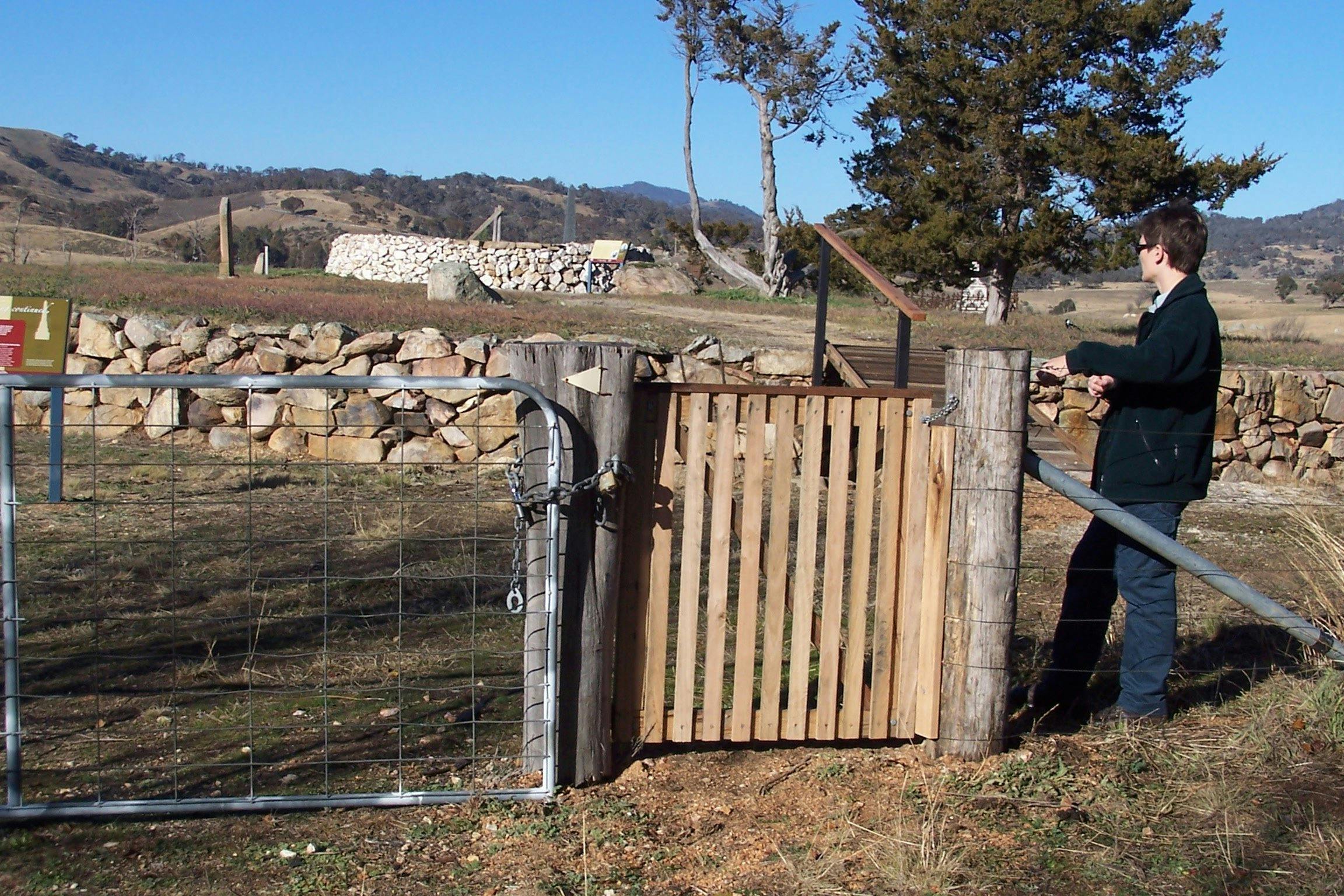 Woman standing at wooden gate looking to background with raised ground and rock walls