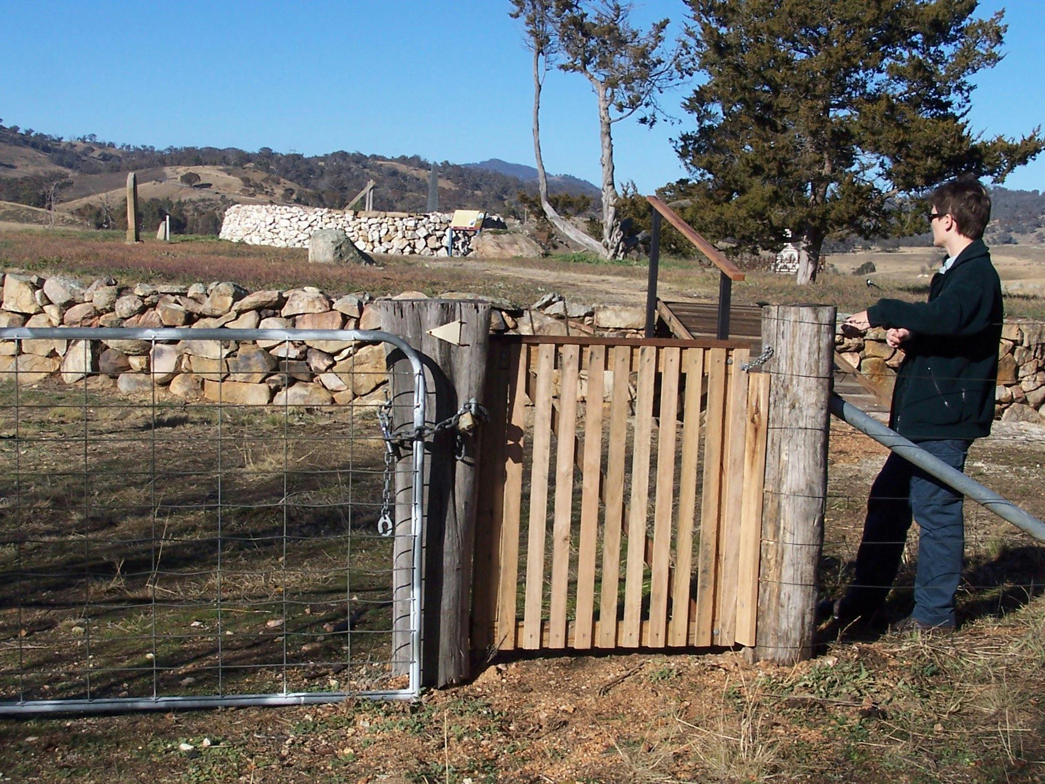 Woman standing at wooden gate looking to background with raised ground and rock walls