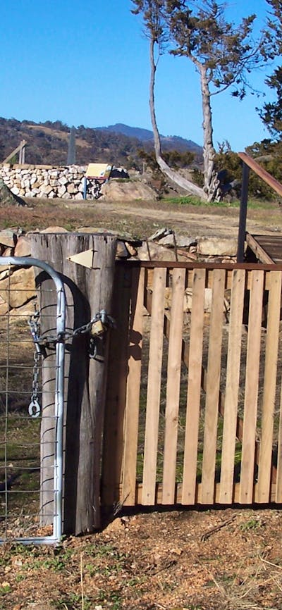 Woman standing at wooden gate looking to background with raised ground and rock walls