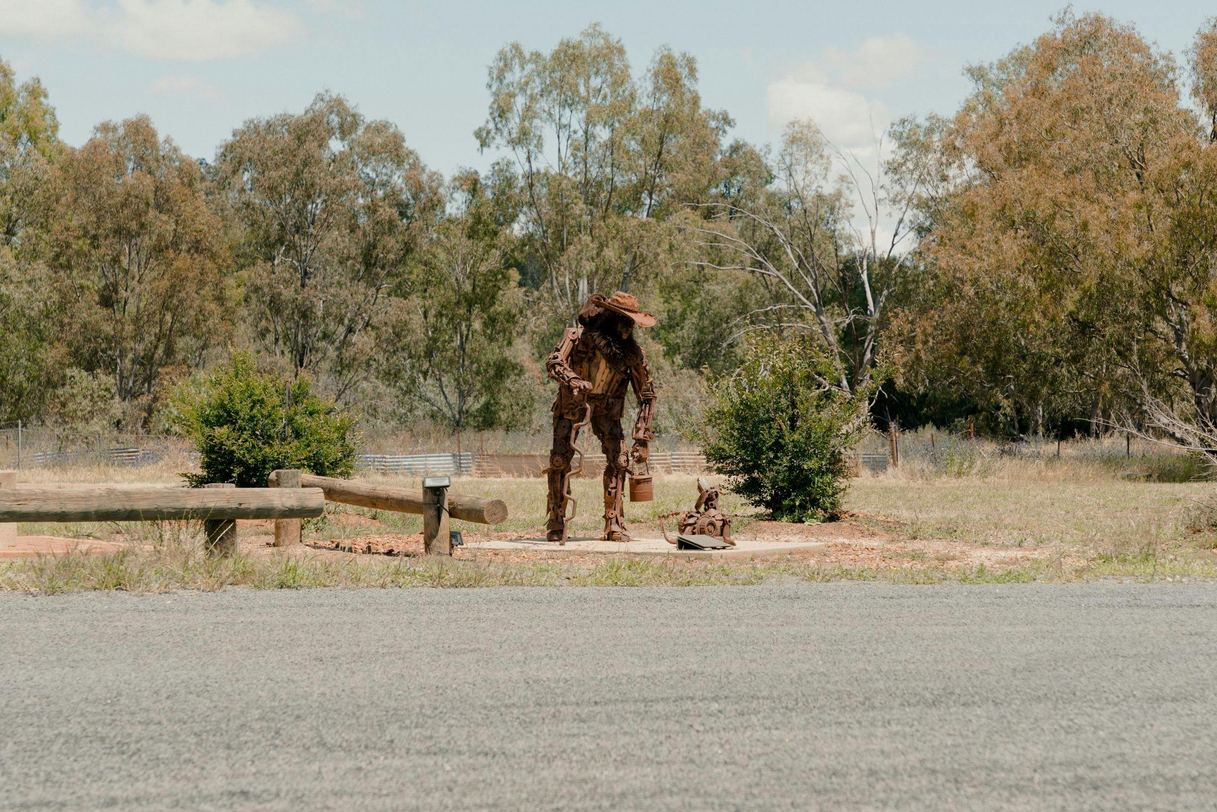 A scrap metal swagman and dog, set in a rural Australian landscape.