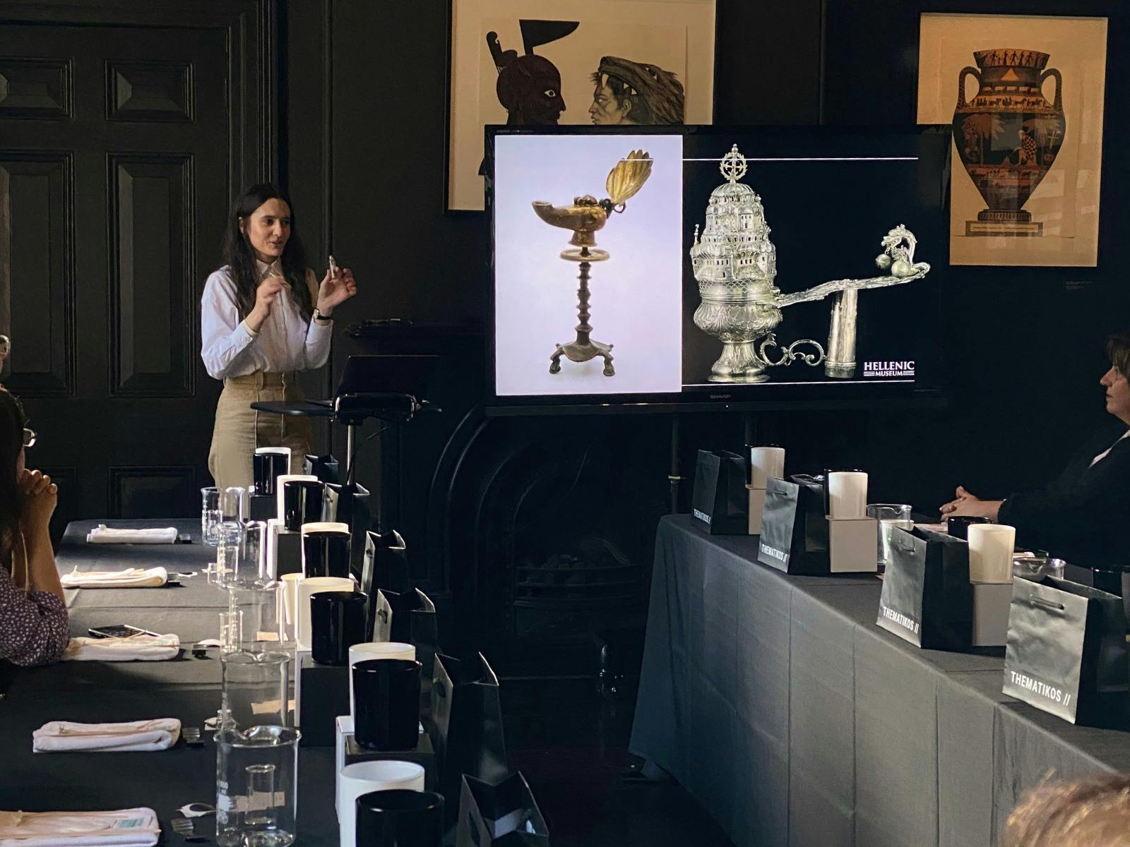 A woman stands in front of a room of workshop attendees talking to slides about historical scents