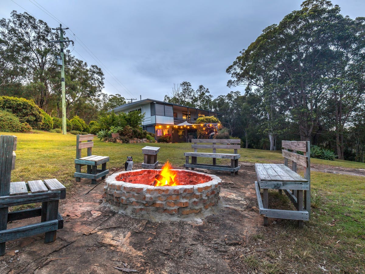 a firepit lit with seating around and house in the distance a firepit lit with seating around and house in the distance