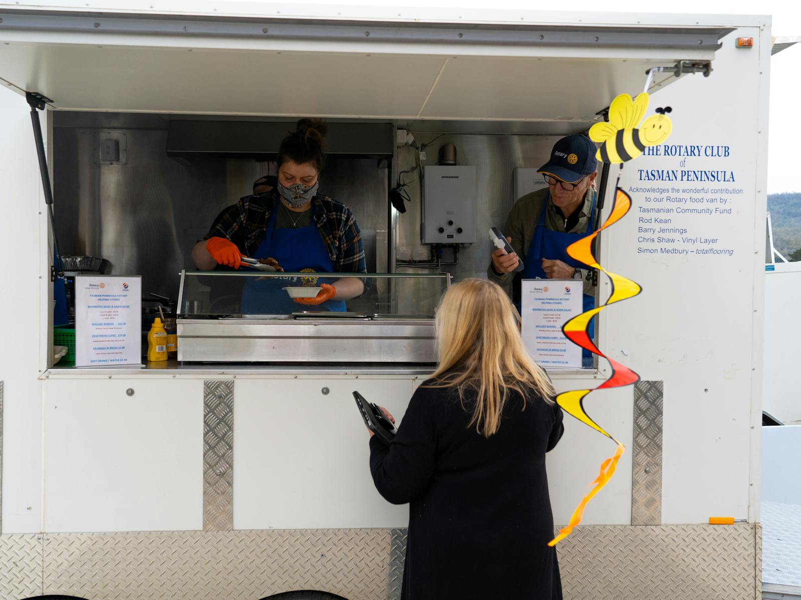 Two Rotarians inside the Rotary van serving up yummy food to a lady enjoying the fine food on offer