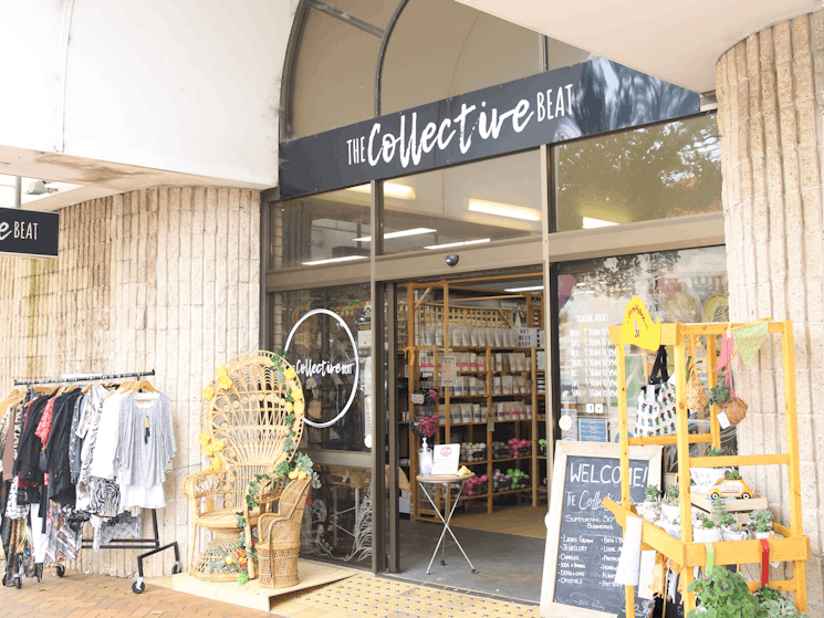 Building with the words The Collective Beat. A clothes rack, cane chair and plants out front