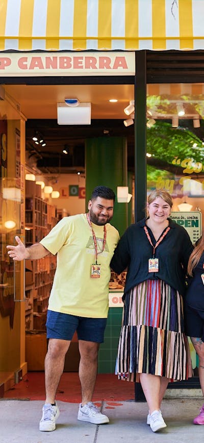A vibrant storefront of POP Canberra with three smiling staff members outside, promoting local goods