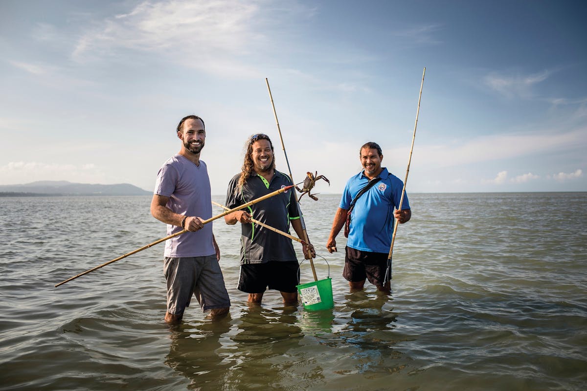 Aboriginal guide standing with guests in knee-deep water, holding spears and crab hunting.