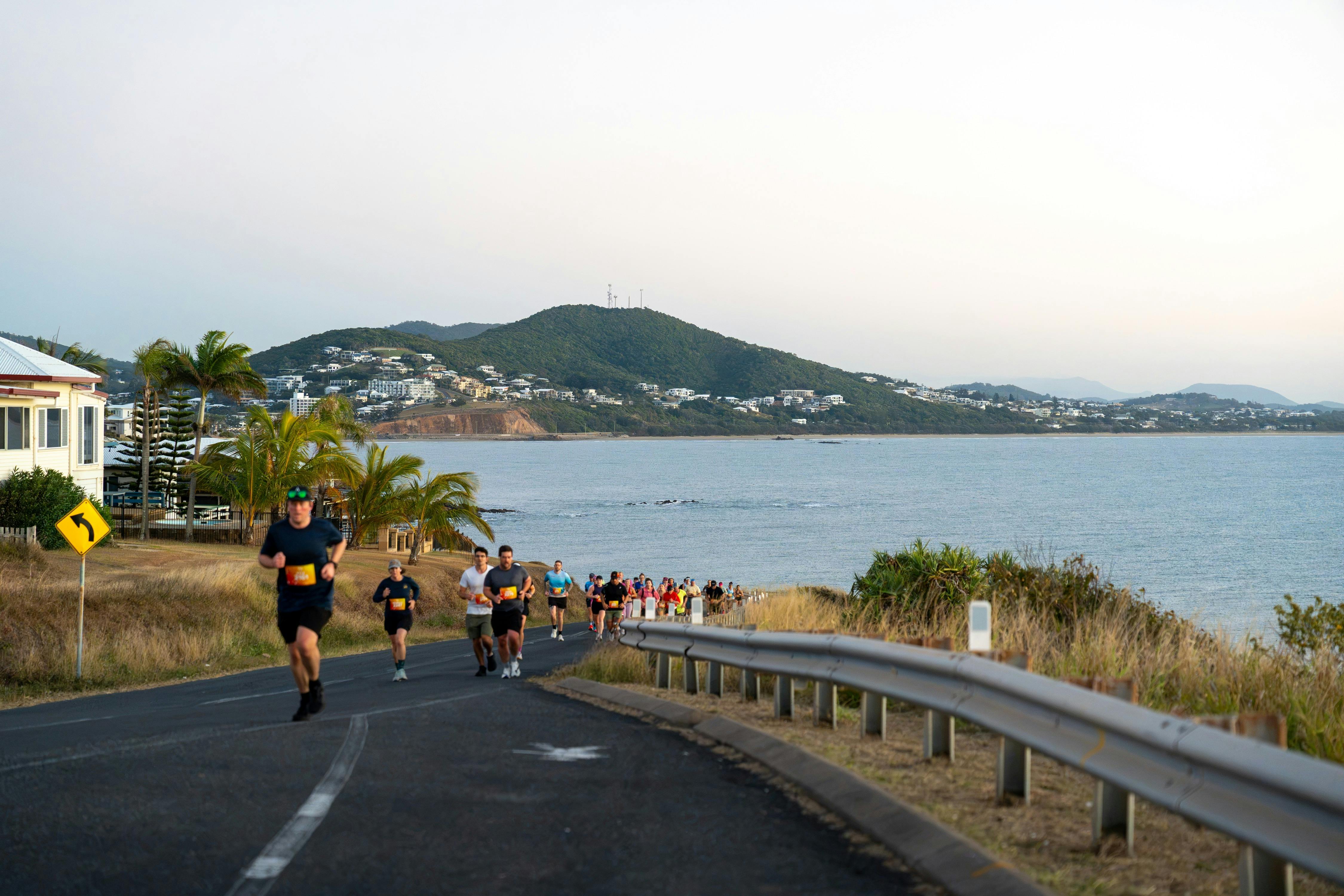 A runner passes spectators beneath coastal pine trees during the Yeppoon Running Festival.