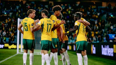Soccer players in yellow kits celebrate a goal on a stadium pitch