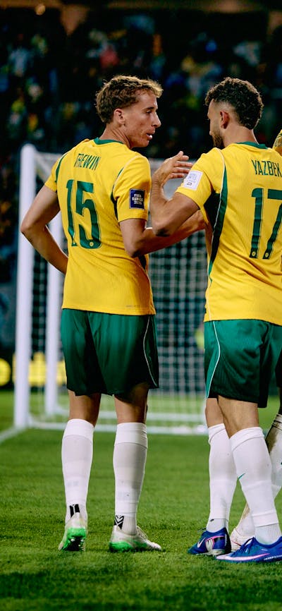 Soccer players in yellow kits celebrate a goal on a stadium pitch
