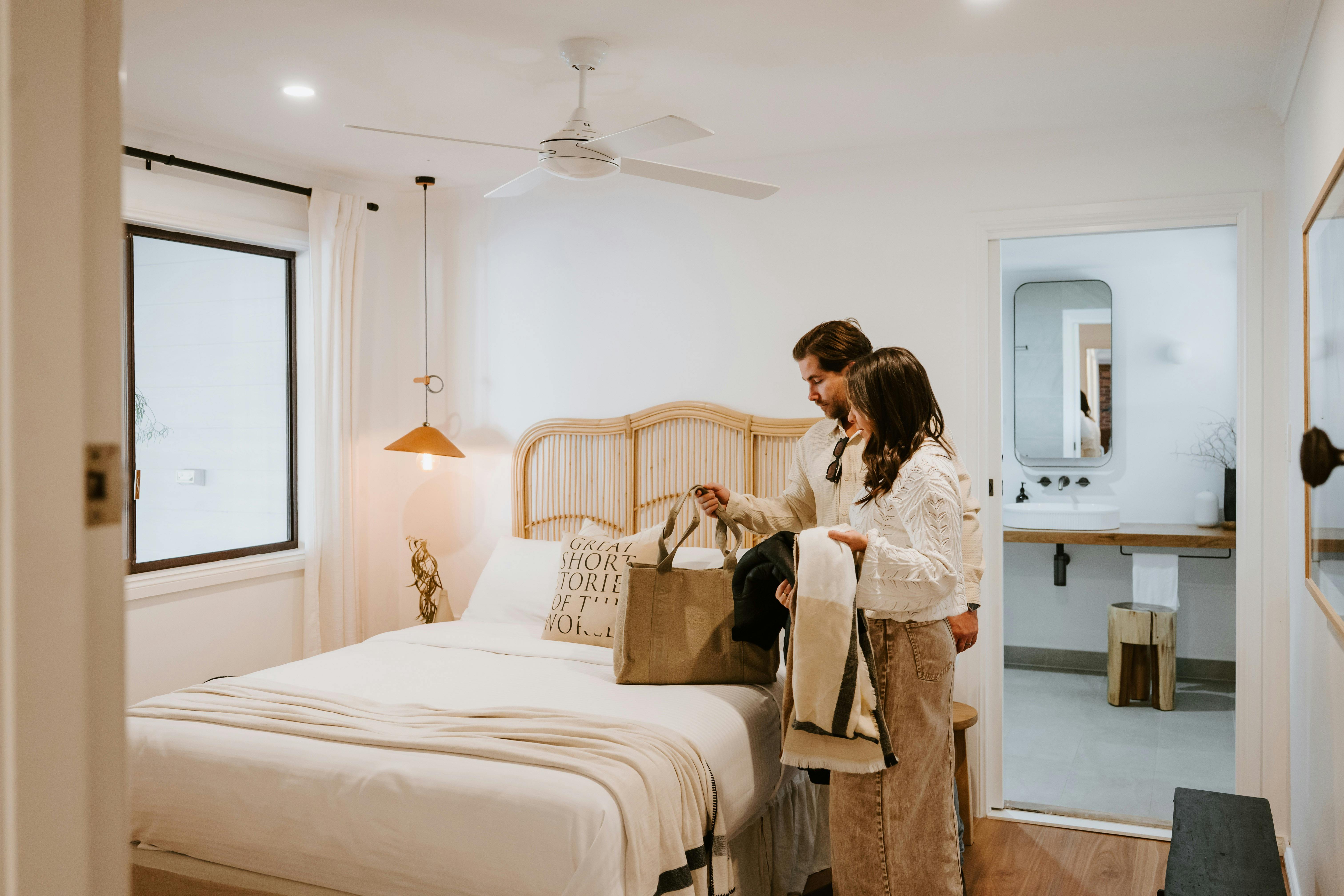 Couple putting shopping bags on bed, ensuite visible in background