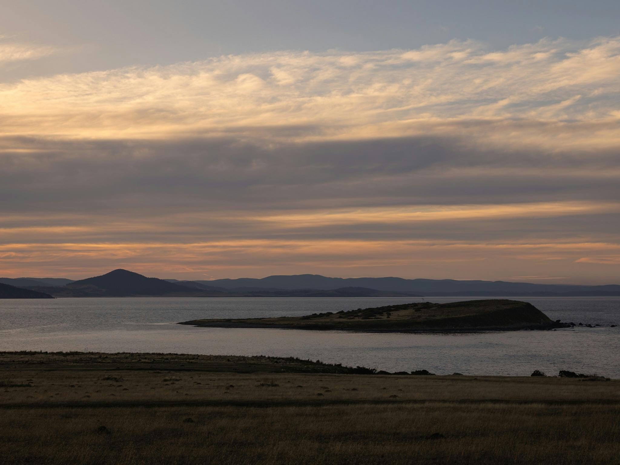 a landscape looking over water with colour in the sky of evening light