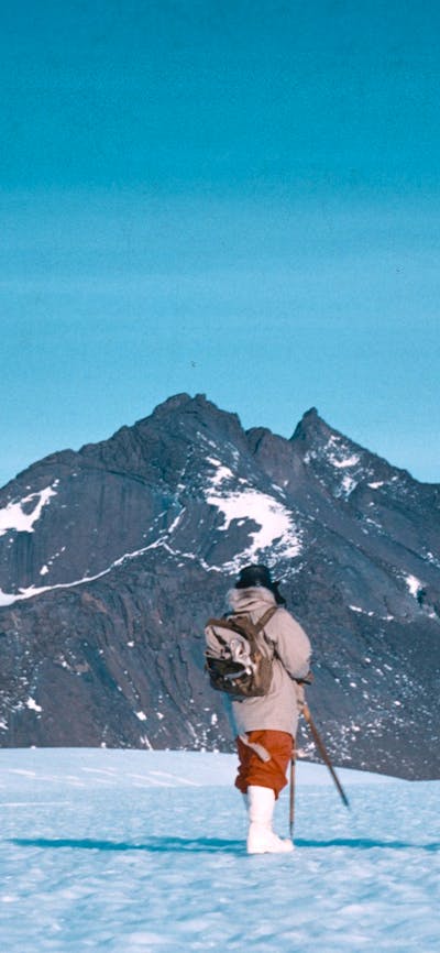 Two hikers trekking across a snow-covered landscape with a mountain in the background.