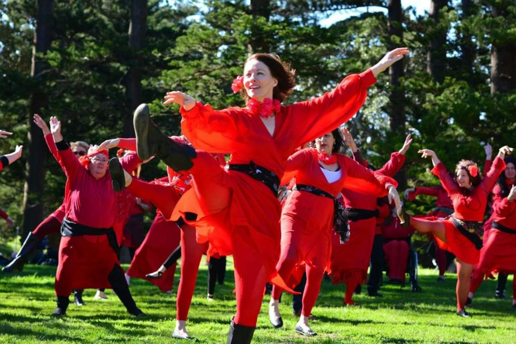 Dancers dressed in red with trees in the background