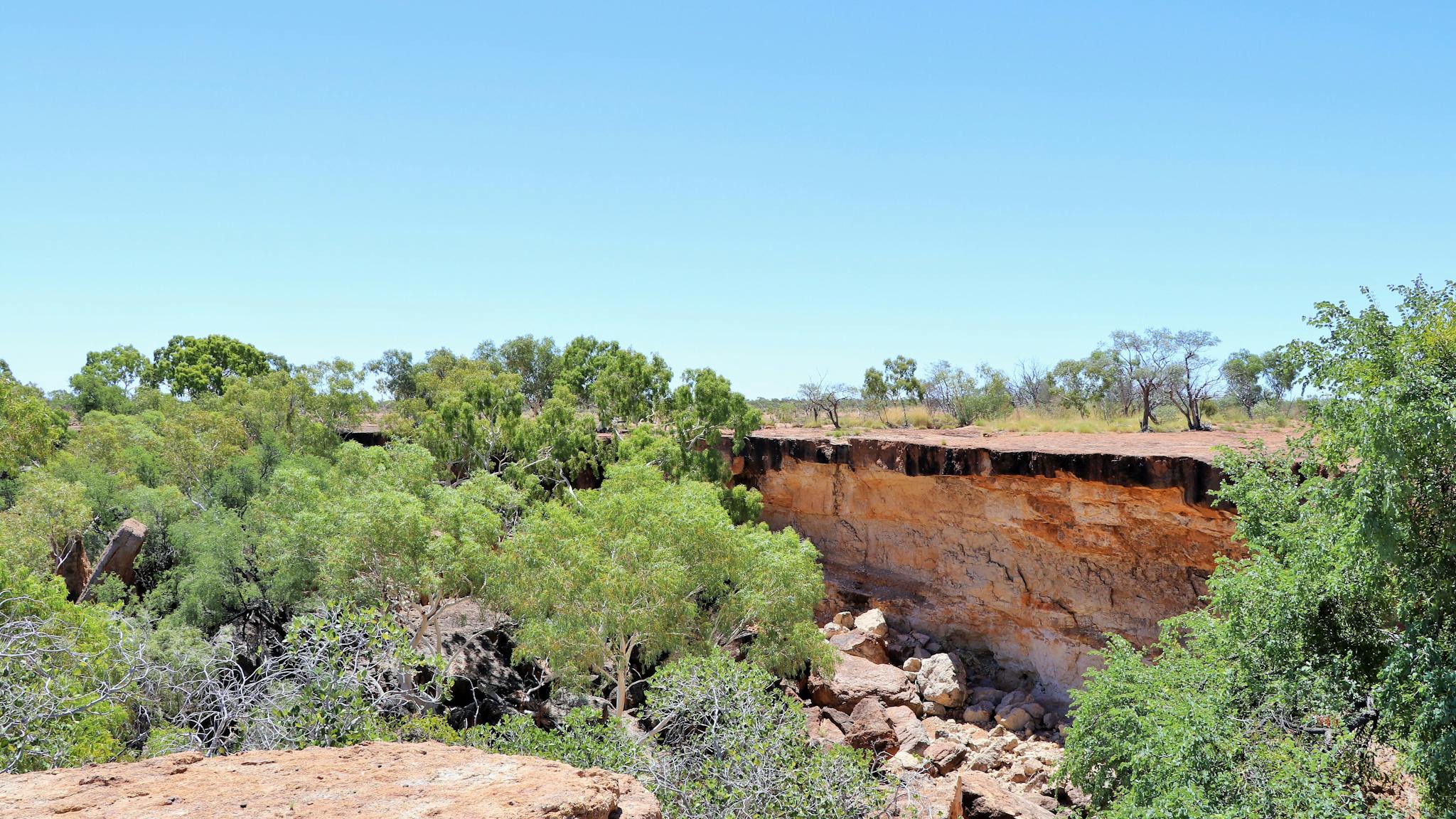 Sandstone cliff edge falling into shallow gorge lined with a few trees and rocks Sandstone cliff edge falling into shallow gorge lined with a few trees and rocks