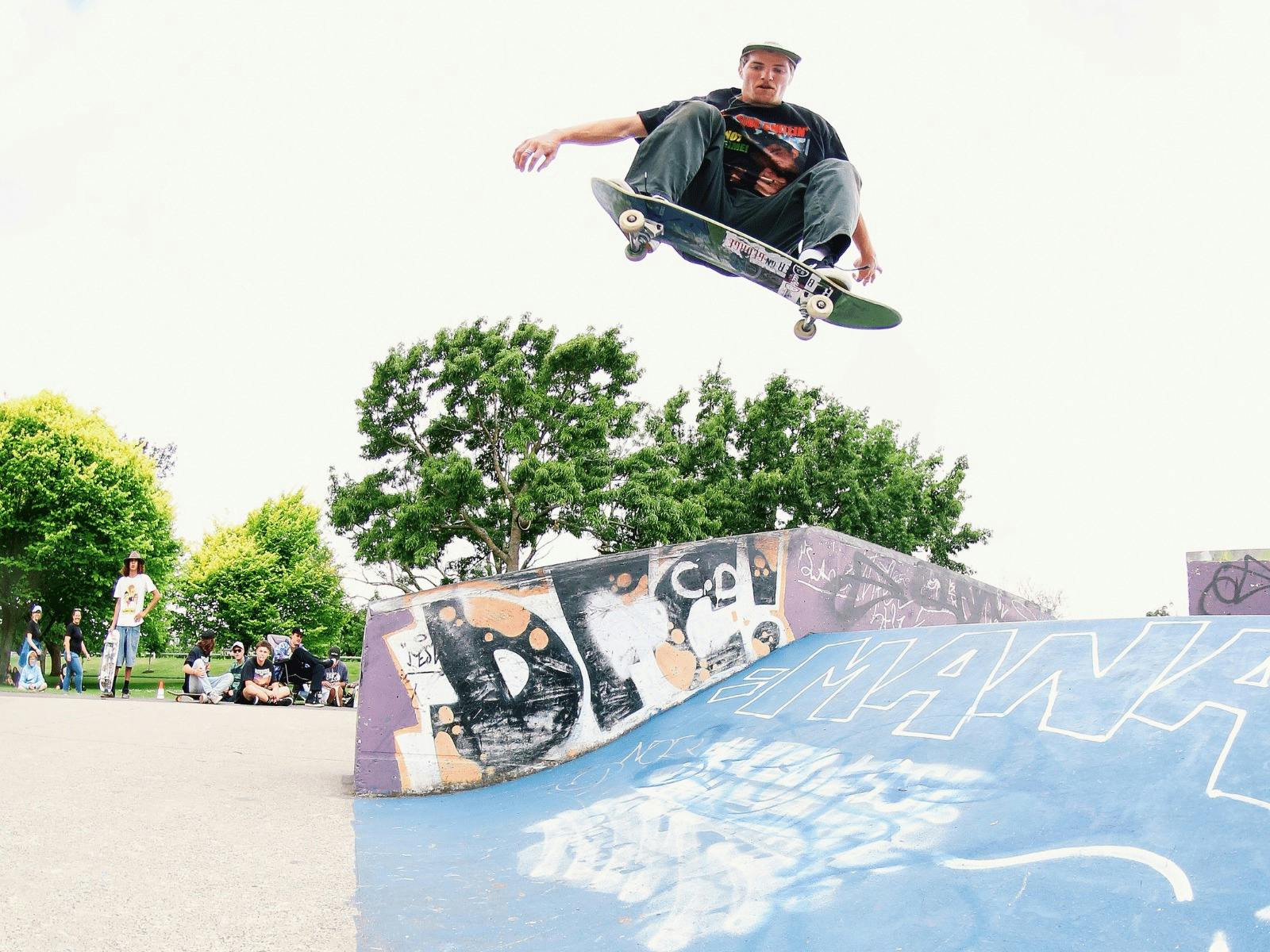 lens is looking up to a skateboarder who is crouched in the air above a skate ramp