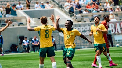 Soccer players in yellow kits celebrate a goal on a stadium pitch as teammates run in behind