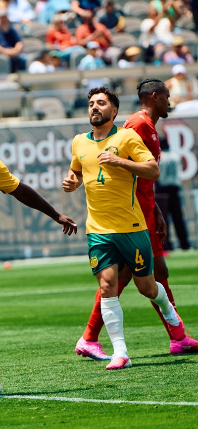 Soccer players in yellow kits celebrate a goal on a stadium pitch as teammates run in behind