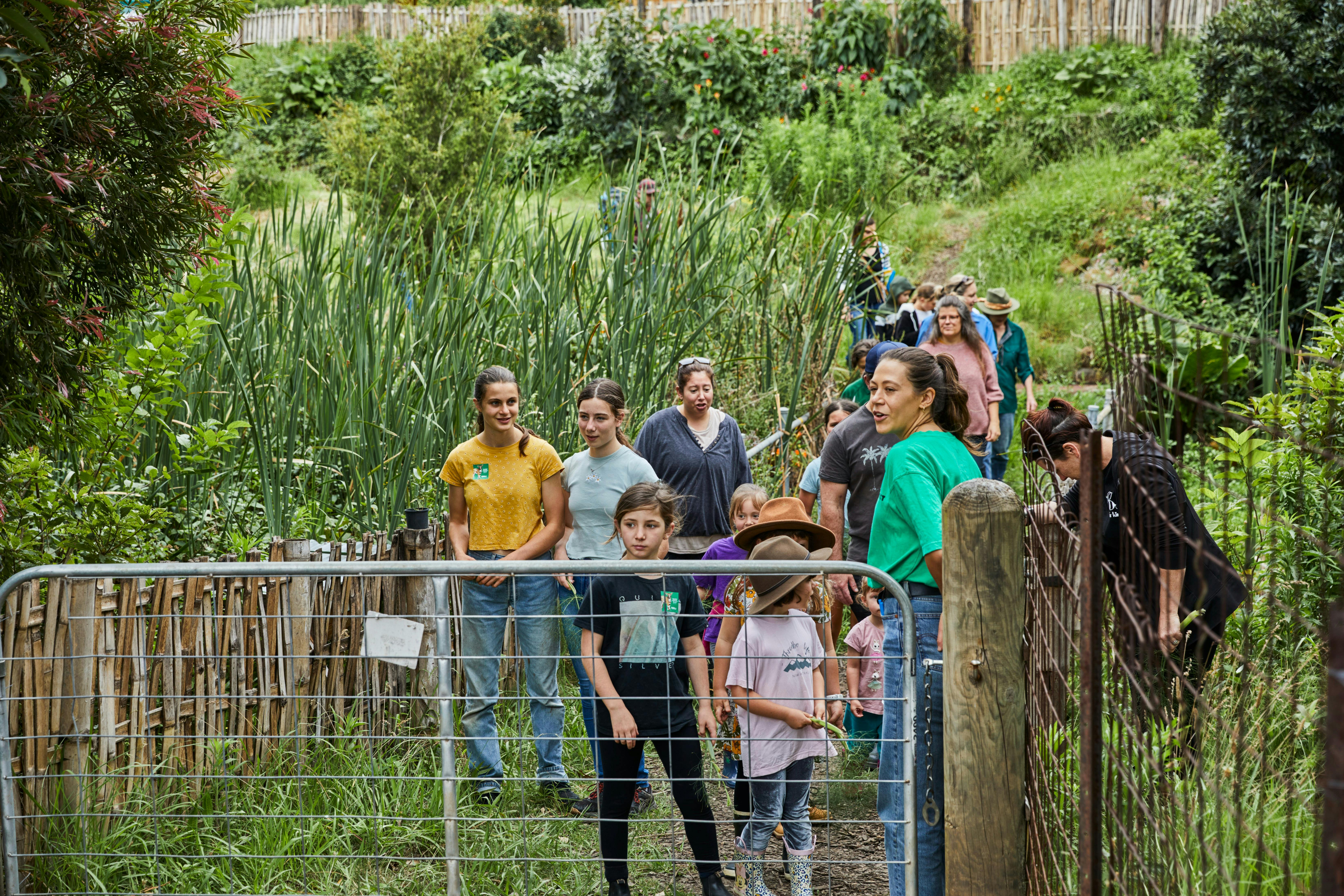 A group of people on a farm tour walk down a garden path to farm gate led by tour guide