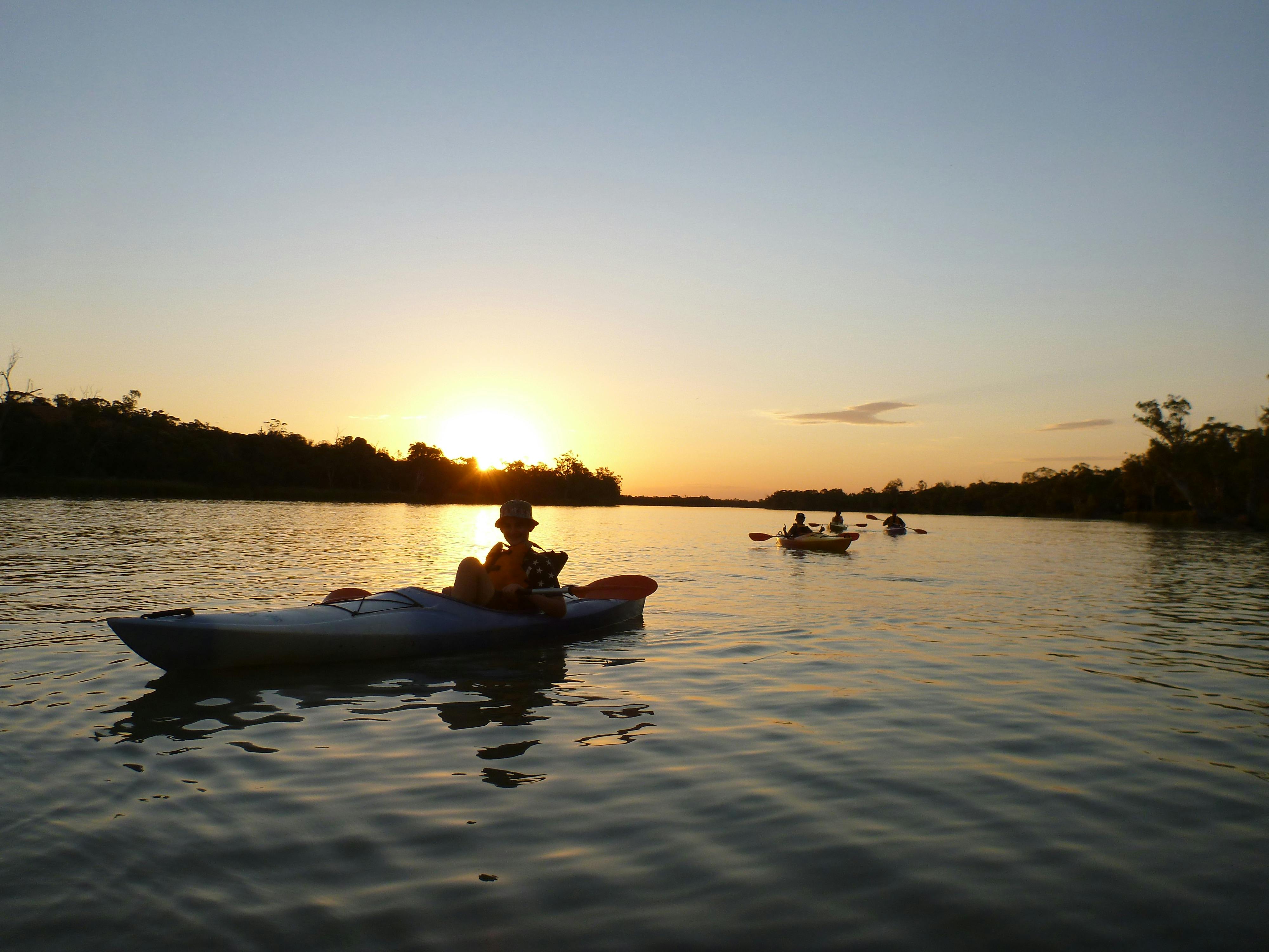 Kayakers in foregroundwiht other kayakers behind in distance.  Golden sunset reflected on water.