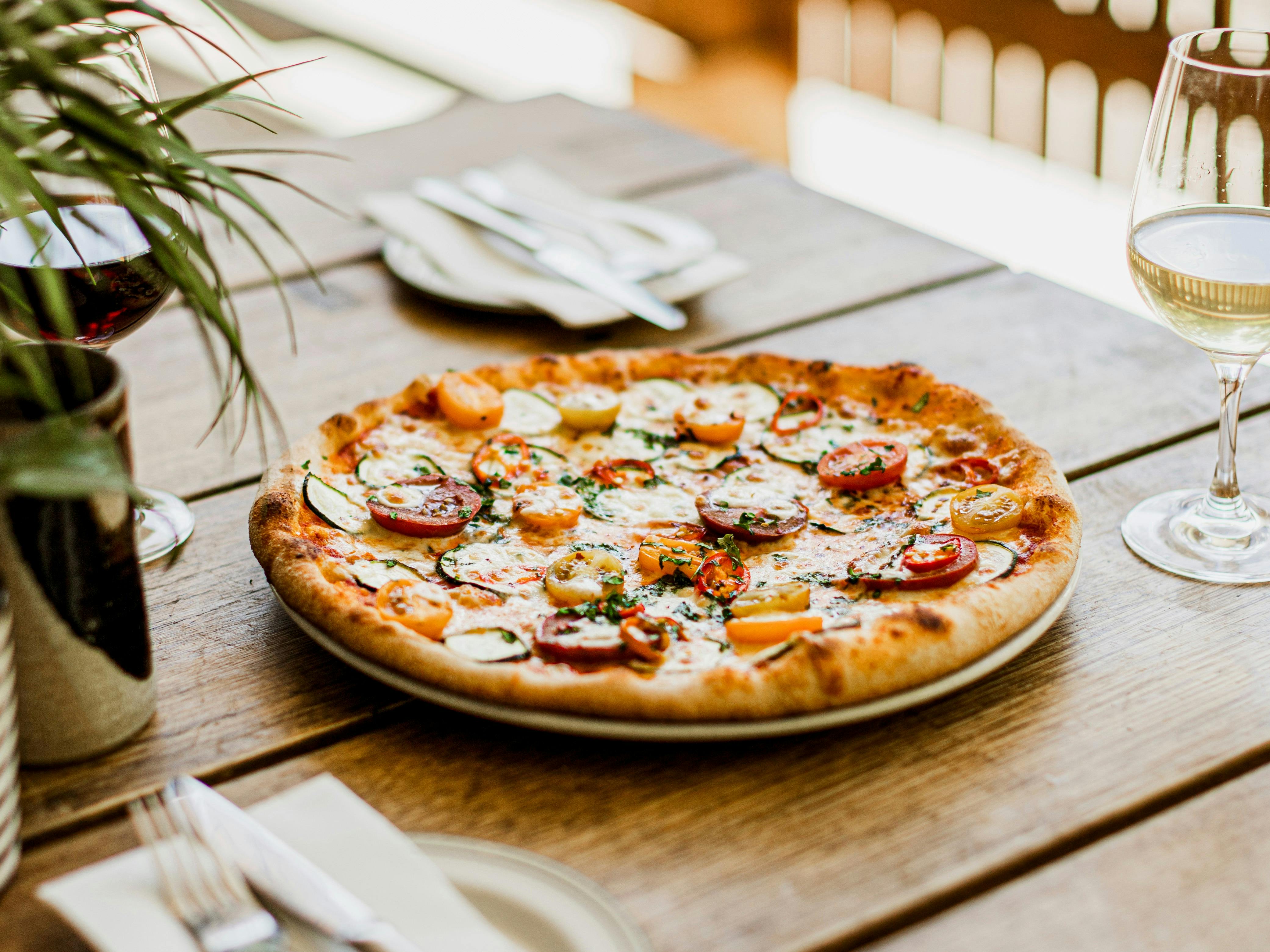 Tomato and zucchini pizza on outdoor table with two glasses of wine