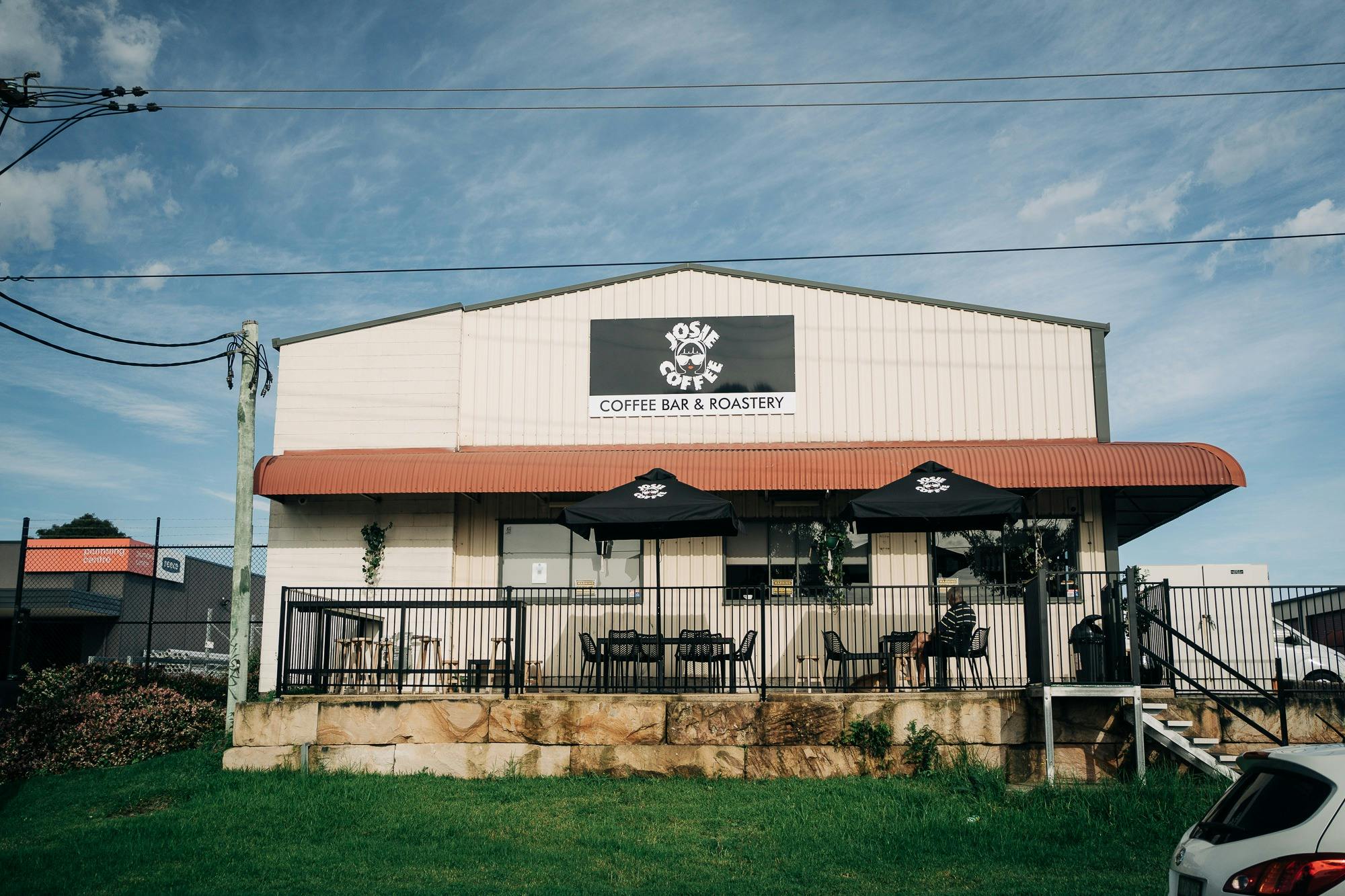 A view of the outside seating at the roastery café. There are cafe umbrellas and a branded sign.