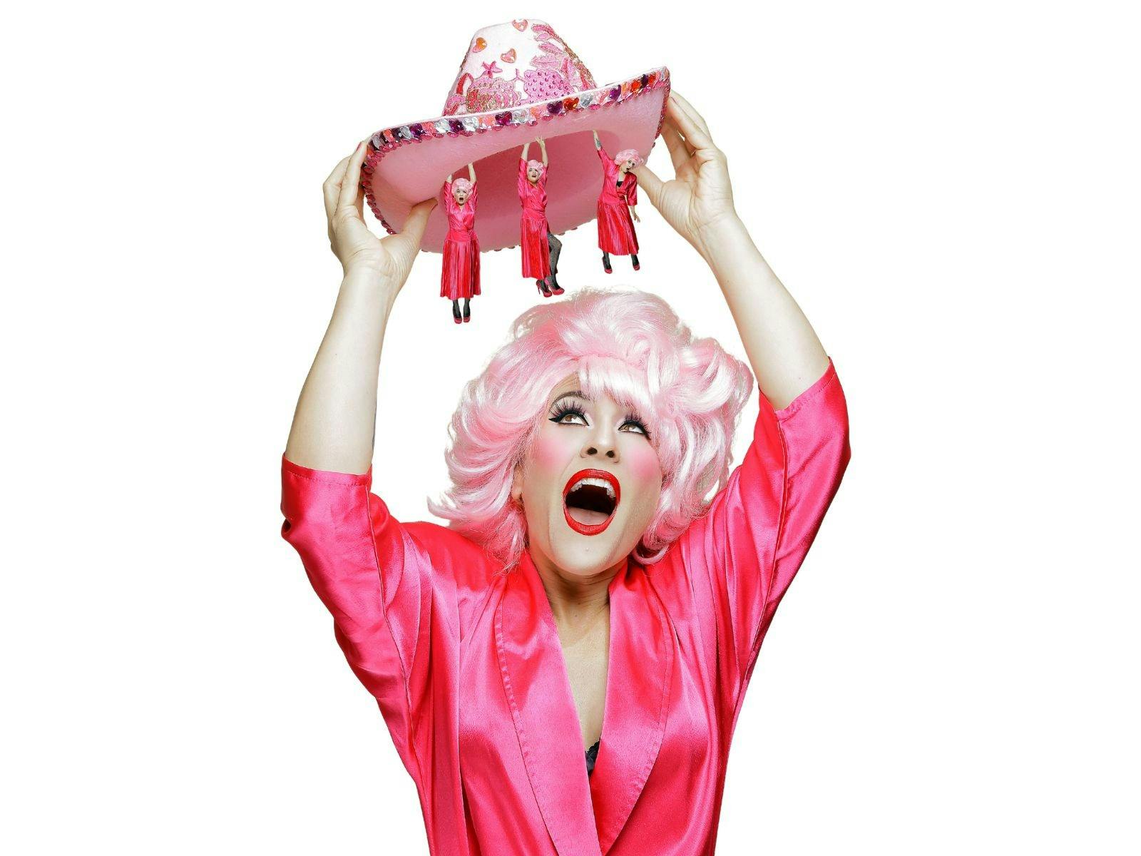 A very camp image of a woman in pink holding up a hat