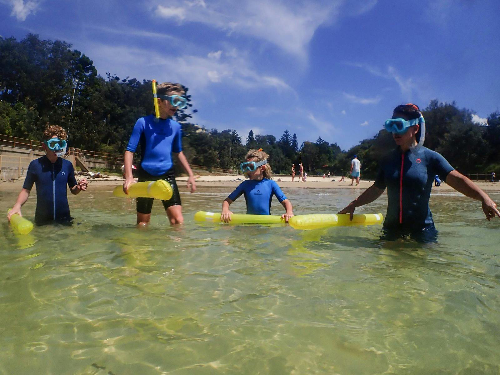Four kids walk into clear water wearing snorkel gear, ready for a snorkeling tour