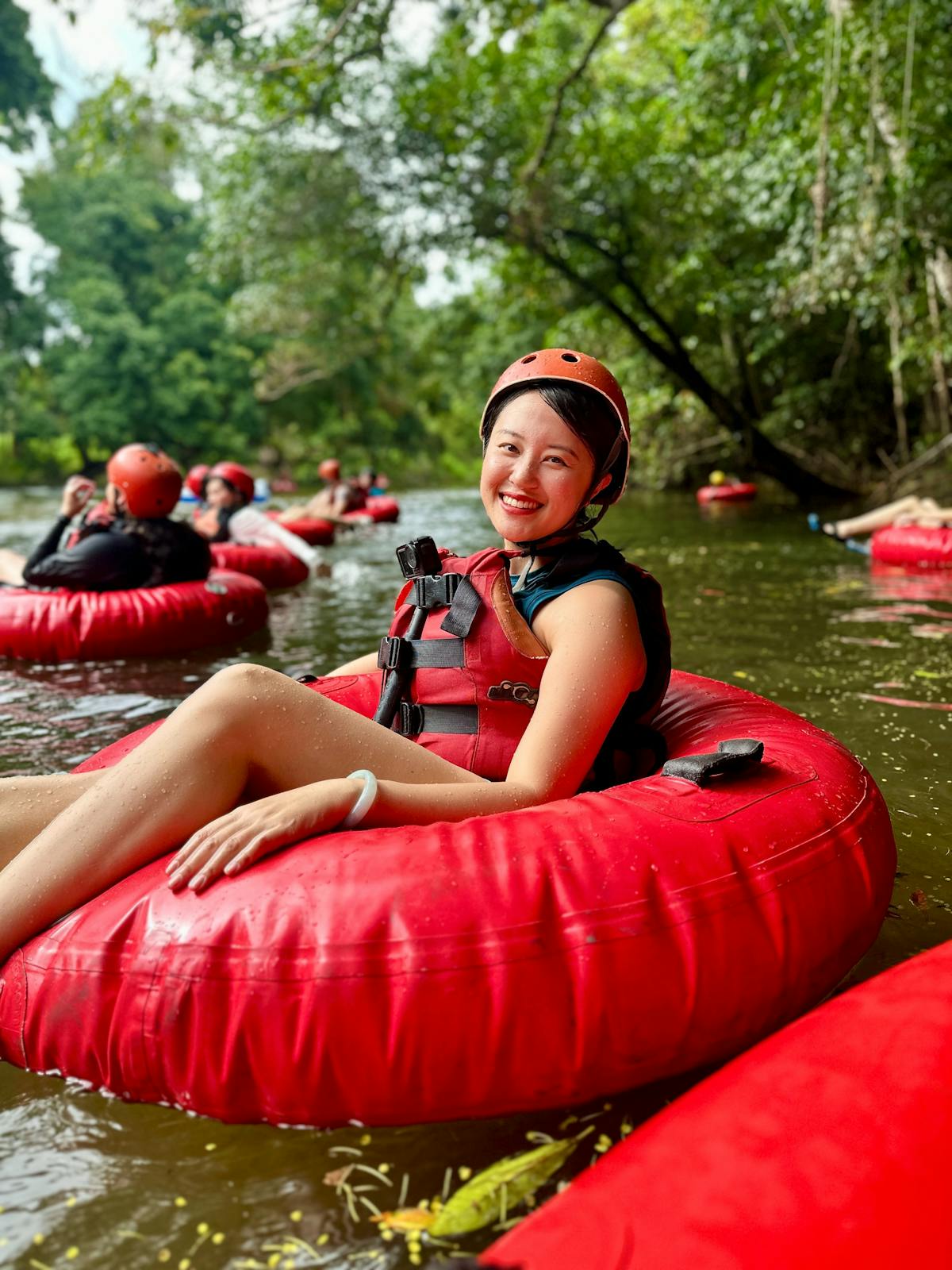 Happy woman wearing a red helmet and life jacket sitting in a red tube on a river in the rainforest