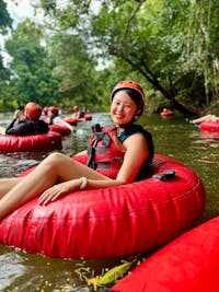 Happy woman wearing a red helmet and life jacket sitting in a red tube on a river in the rainforest