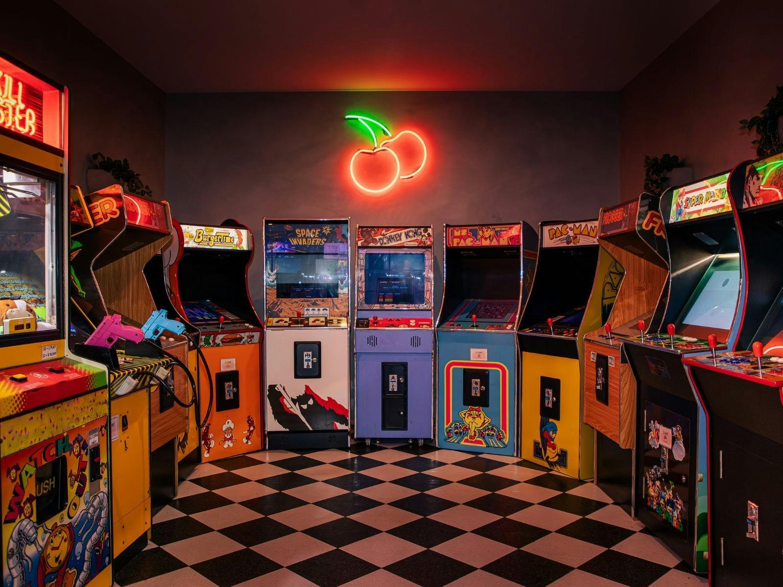 A room full of retro arcade games with a cherry LED sign