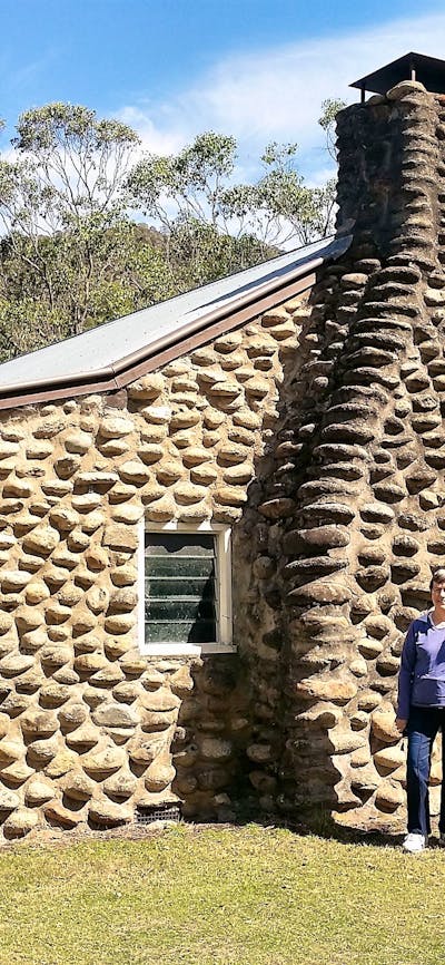 two women standing in front of hut made from river rock