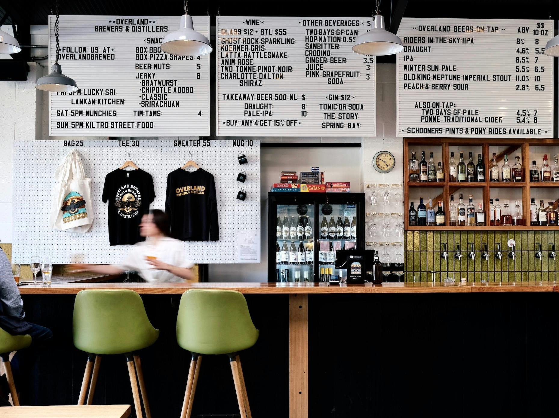 Overland taproom bar scene  with hanging menu boards, beer taps, bar and green stools