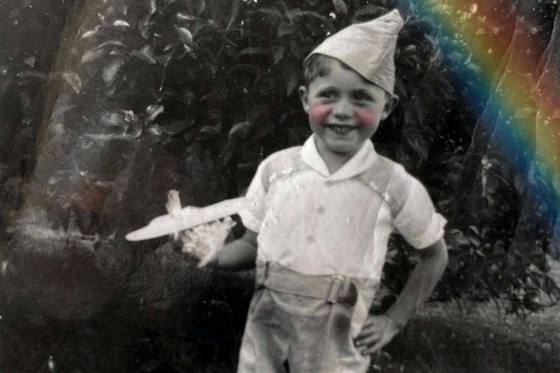 A black and white image with a colour rainbow in the corner. A young boy from the 50s holds a plane