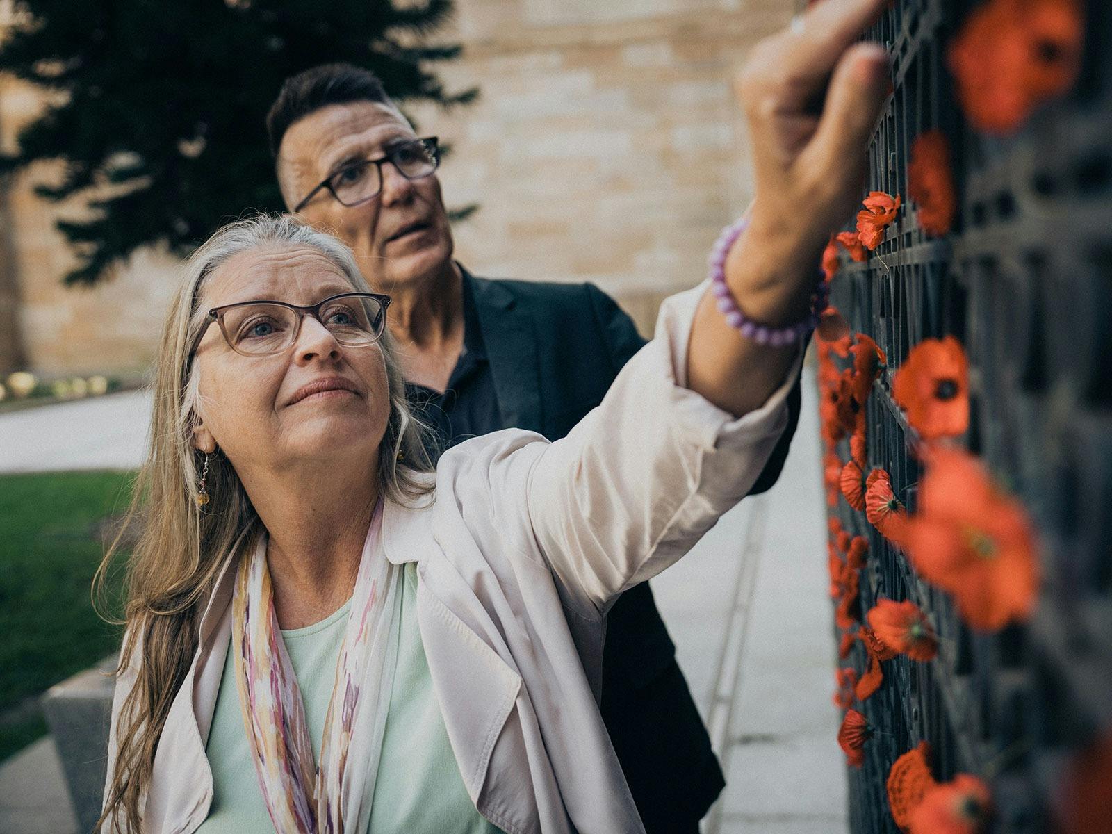 Couple placing a poppy on the commemorative screens outside in the Anzac Square parklands