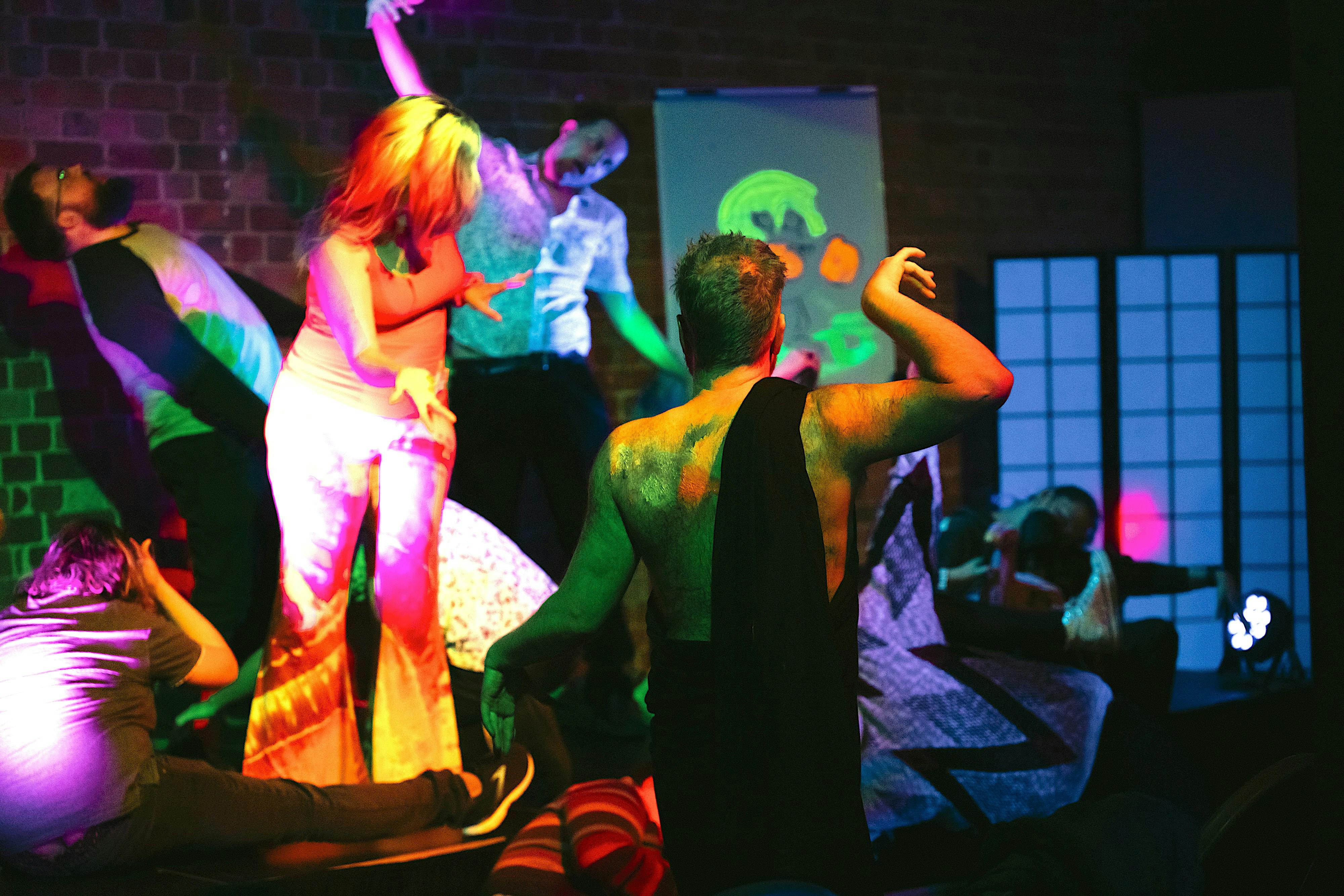 Multiple people are in a theatre space dancing under UV light