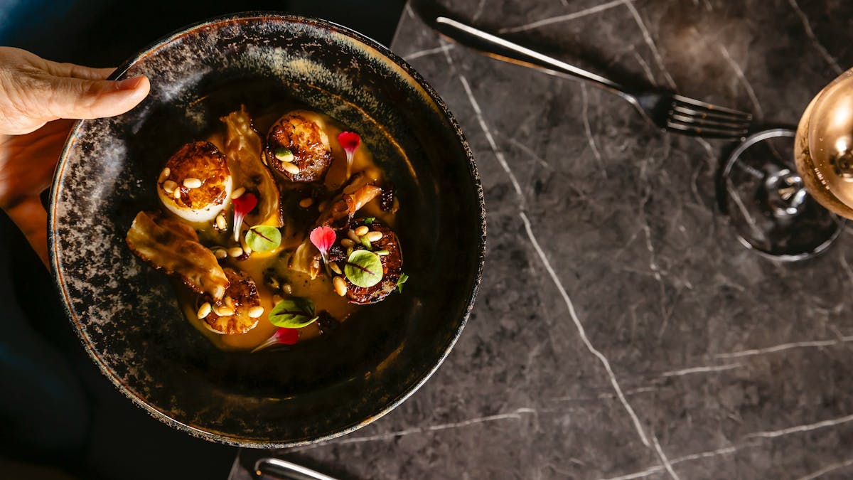 Top view from a dark plate with pan seared scallops being served on a table