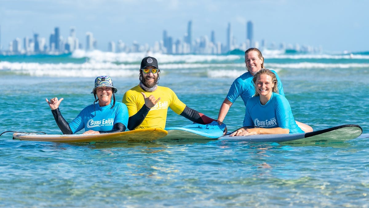 3 women and one male surf instructor smiling in ocean.