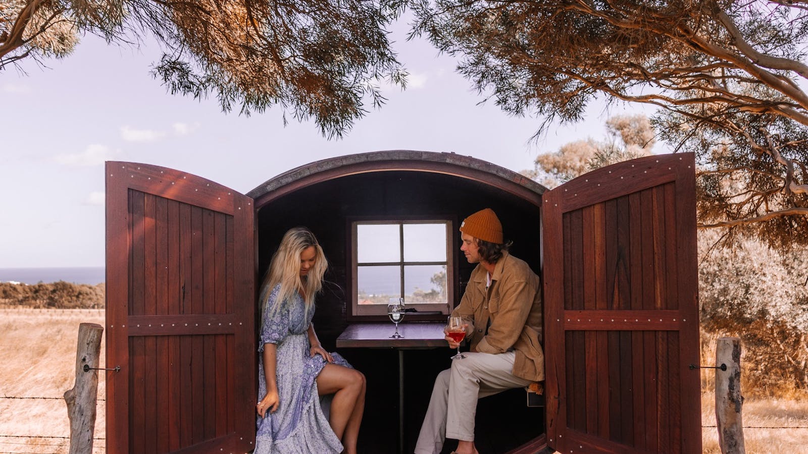 Two people sitting inside the wine barrel pod, overlooking the ocean