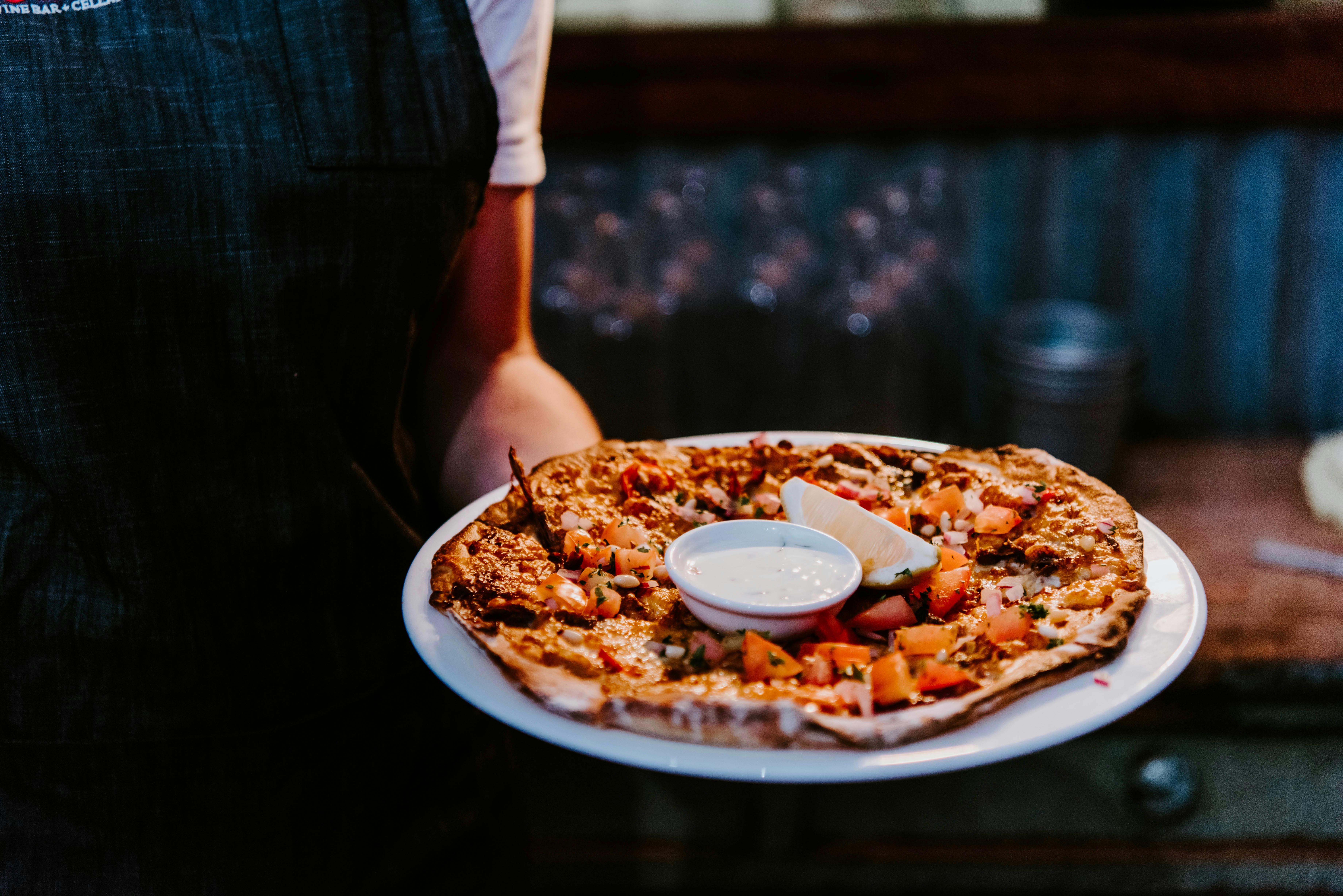 Waitress holding wood-fired middle eastern lamb pizza