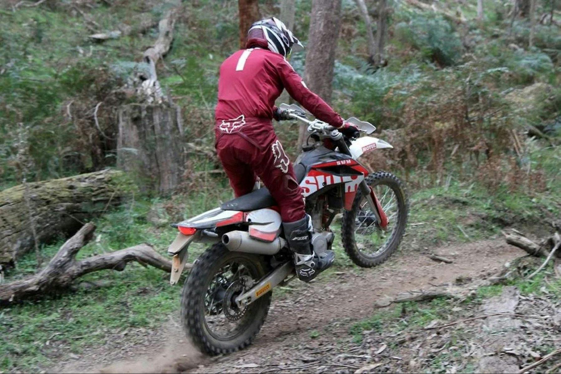 person in a red race suite with a helmet riding a dirt bike in the forest