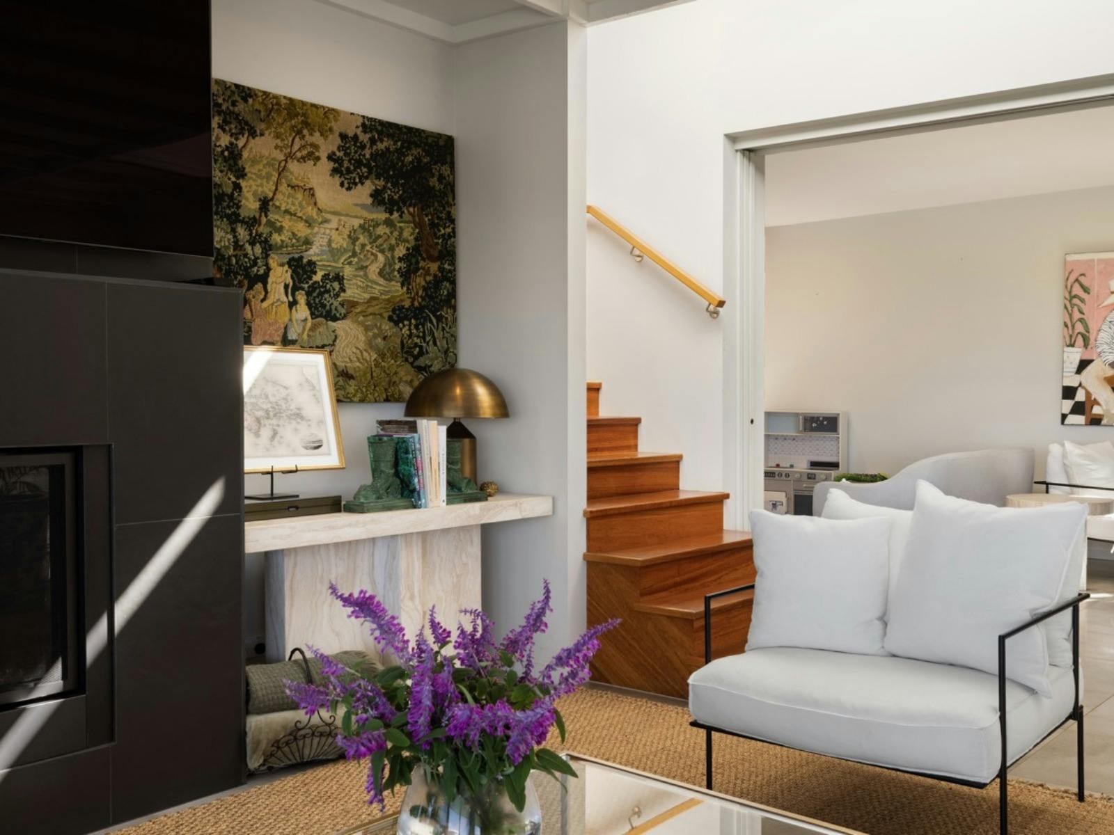 Living area featuring fireplace, artwork, timber staircase and designer furnishings.