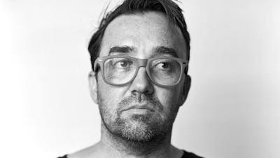 A sepia portrait of a man with glasses, looking slightly upward and to the side.