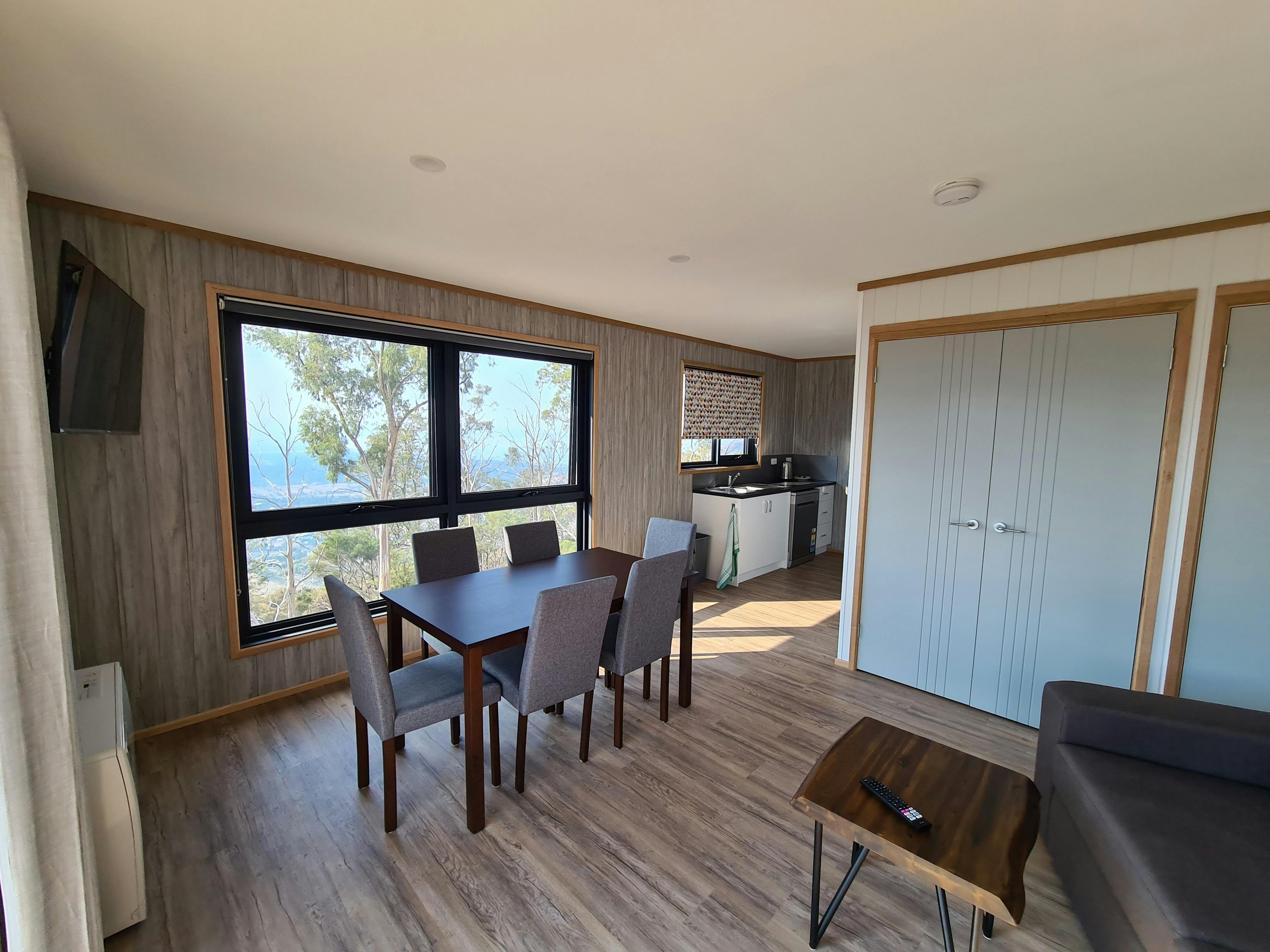 Dining table and chairs beside large windows overlooking the landscape