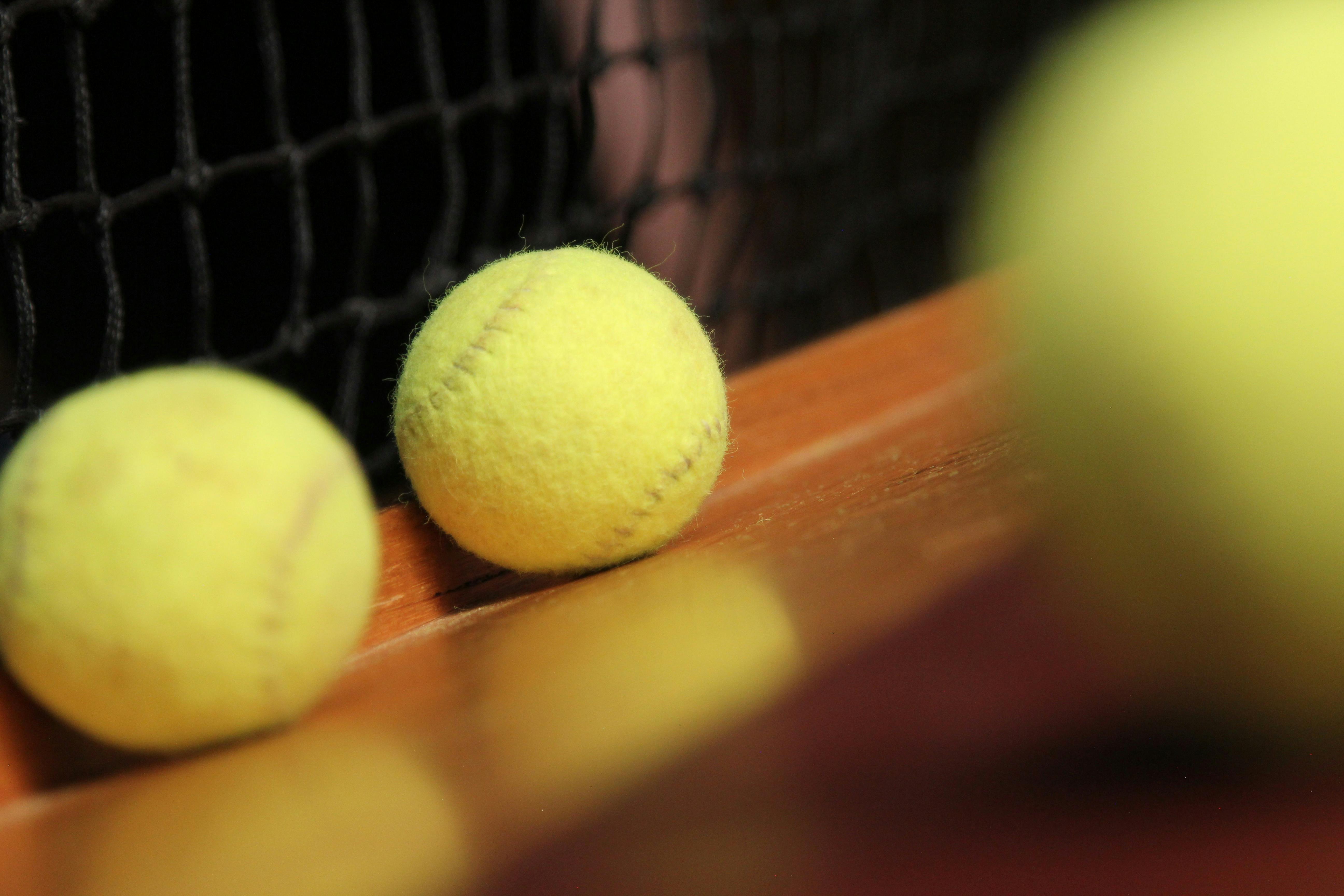 Three hand made yellow tennis balls lie on a wooden platform with a net behind.