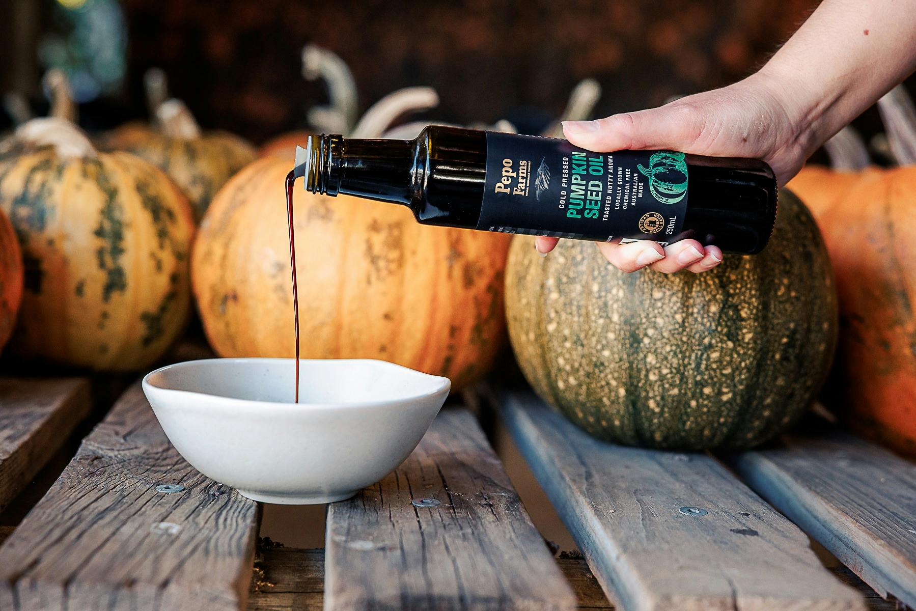 Pumpkin seed oil being poured into a bowl in front of harvested heirloom pumkins