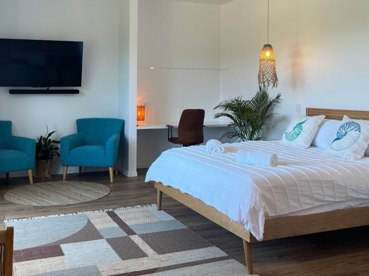 Bedroom with King size bed, two blue arm chairs, large TV and study nook