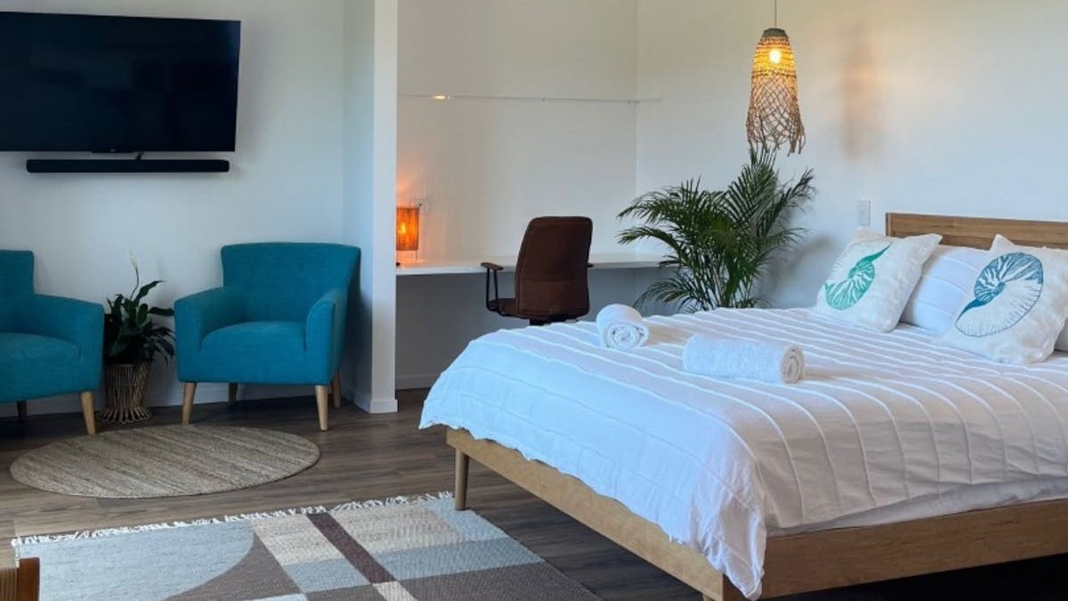 Bedroom with King size bed, two blue arm chairs, large TV and study nook