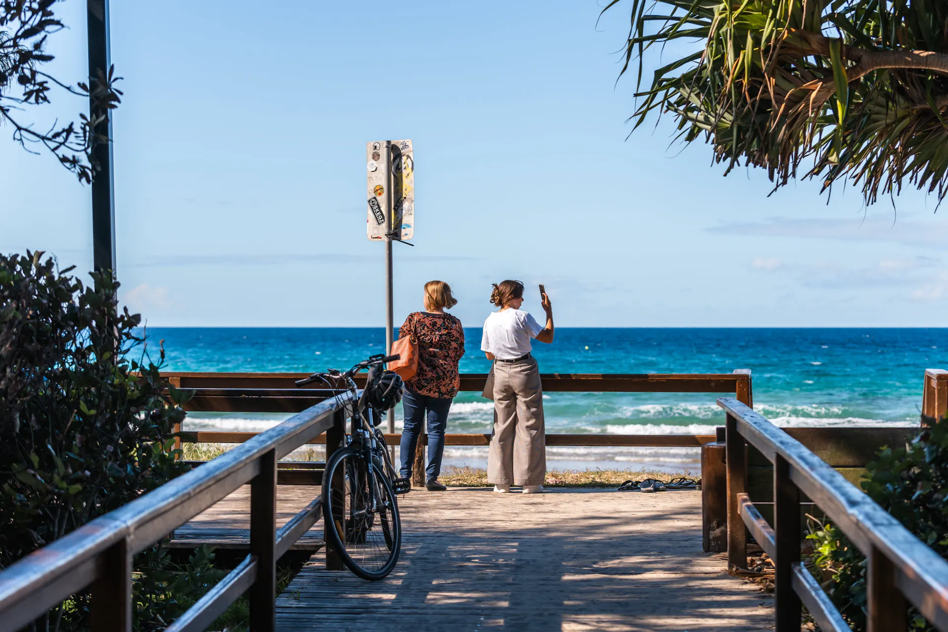 Shot of 2 women at the end of a small boardwalk with ocean in the background. Mudjimba Park entrance