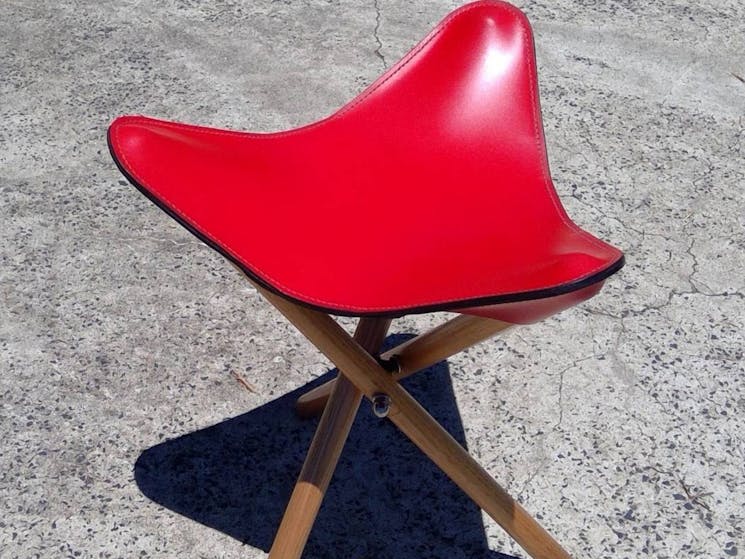 A red leather fold-up stool with three timber legs